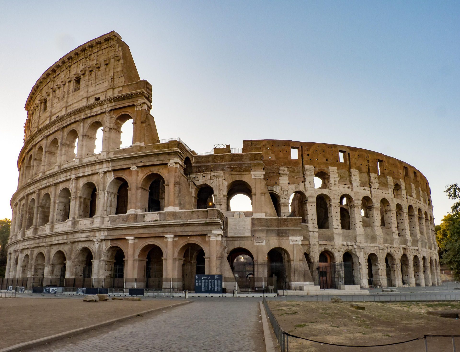 Vista exterior del Coliseo Romano bajo el cielo claro, mostrando la estructura de piedra antigua con sus arcos característicos y los restos de sus niveles superiores.