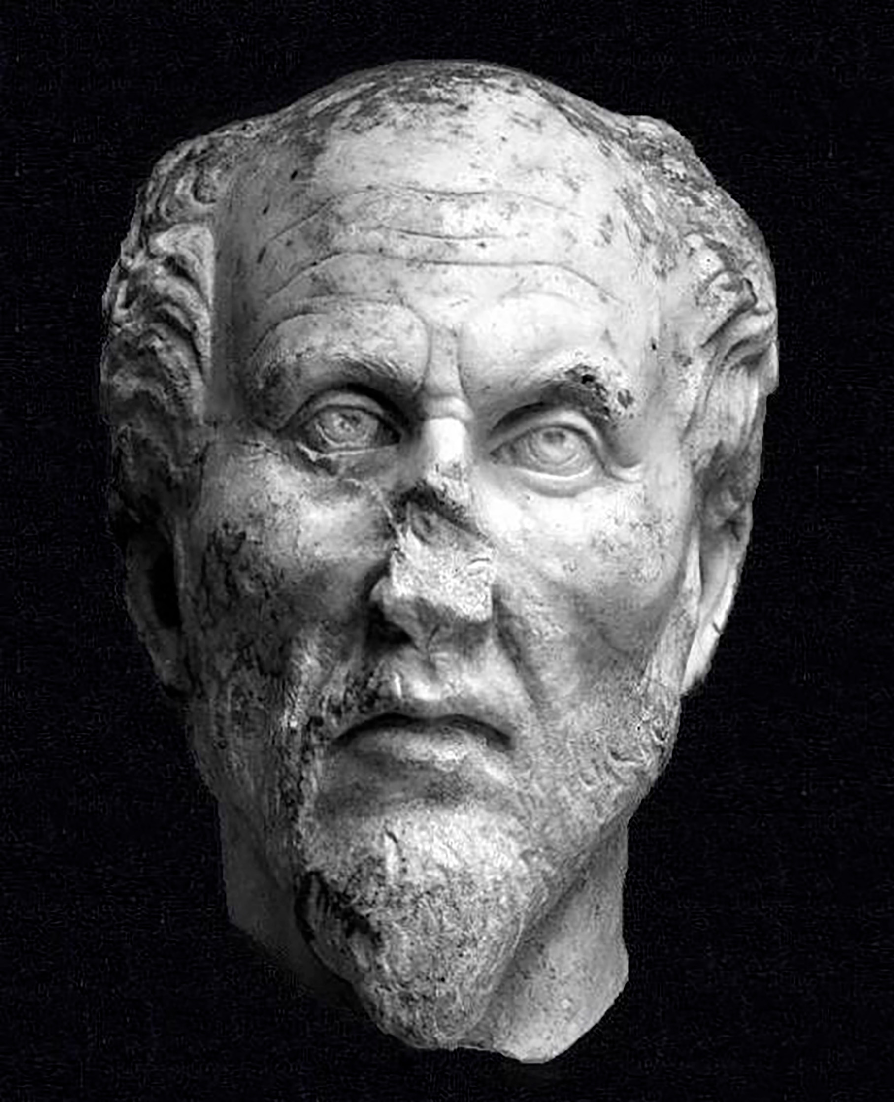 Busto de mármol de la época romana que representa al filósofo Plotino, con frente prominente, arrugas marcadas, barba corta y daños visibles en el puente de la nariz.