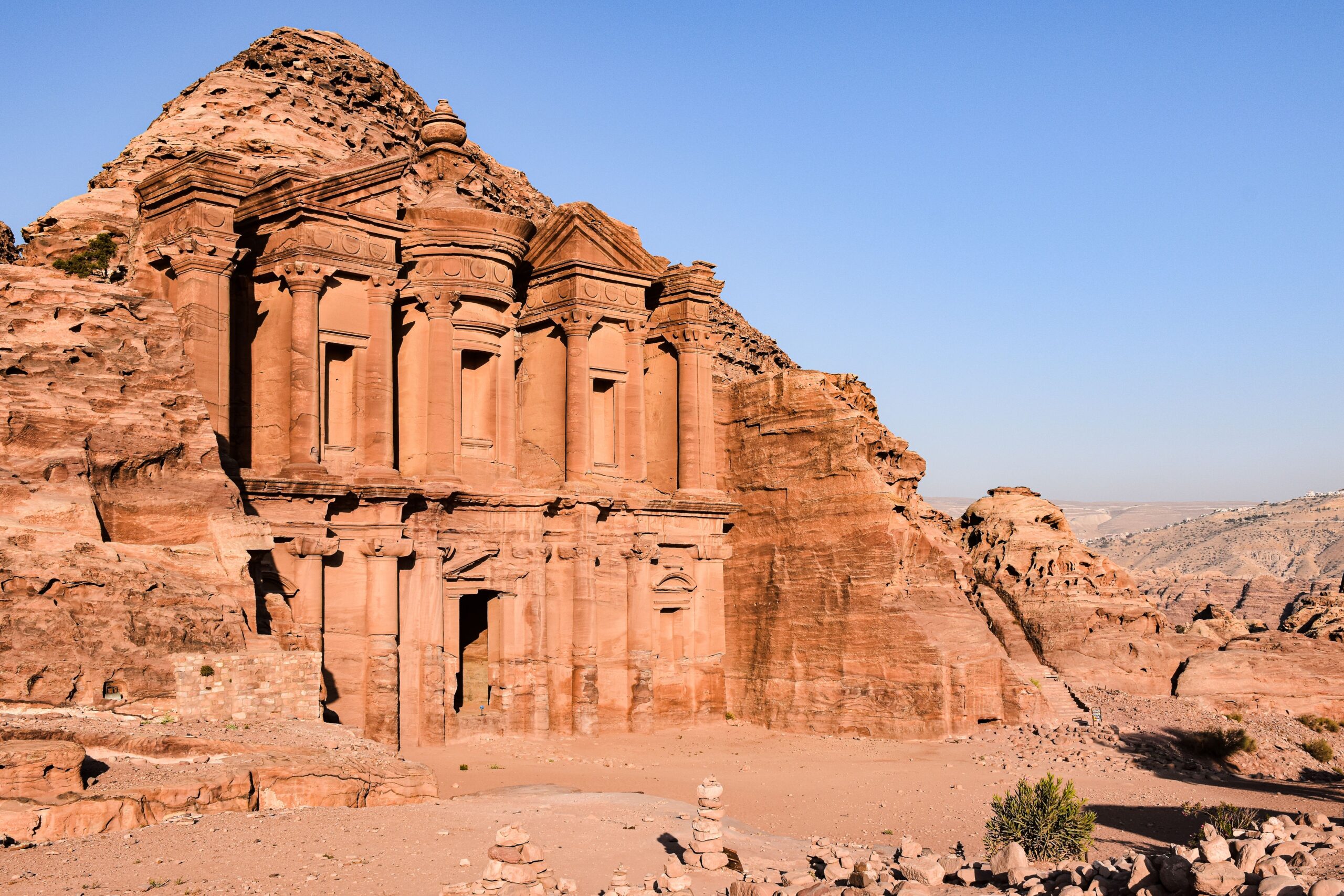 Fachada monumental de piedra de El Monasterio esculpida en una montaña de arenisca rojiza en Petra bajo un cielo azul claro.