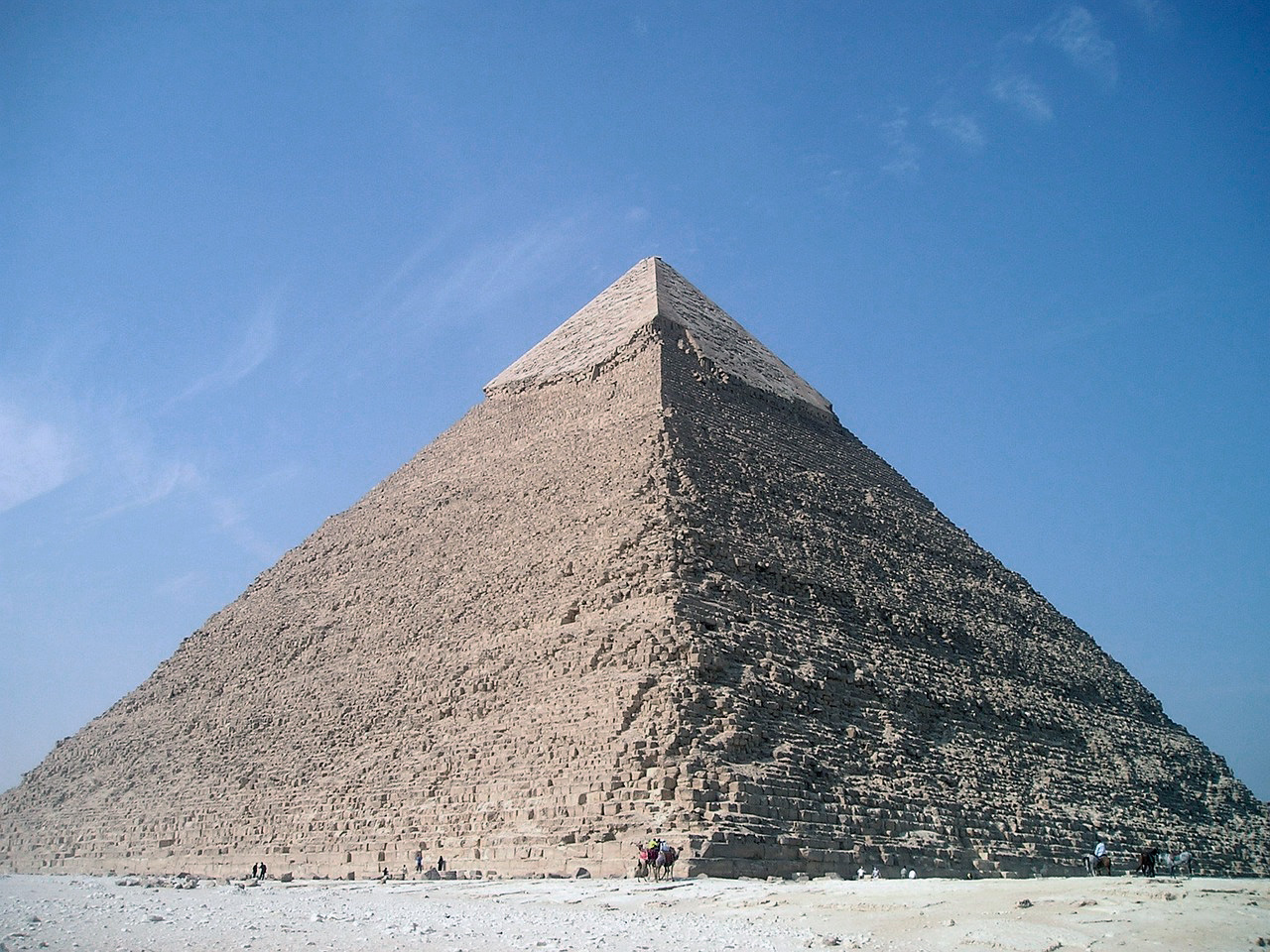 Vista de la Pirámide de Giza perteneciente al faraón Jafra, destacando el revestimiento original de piedra caliza en su cúspide bajo un cielo azul despejado.