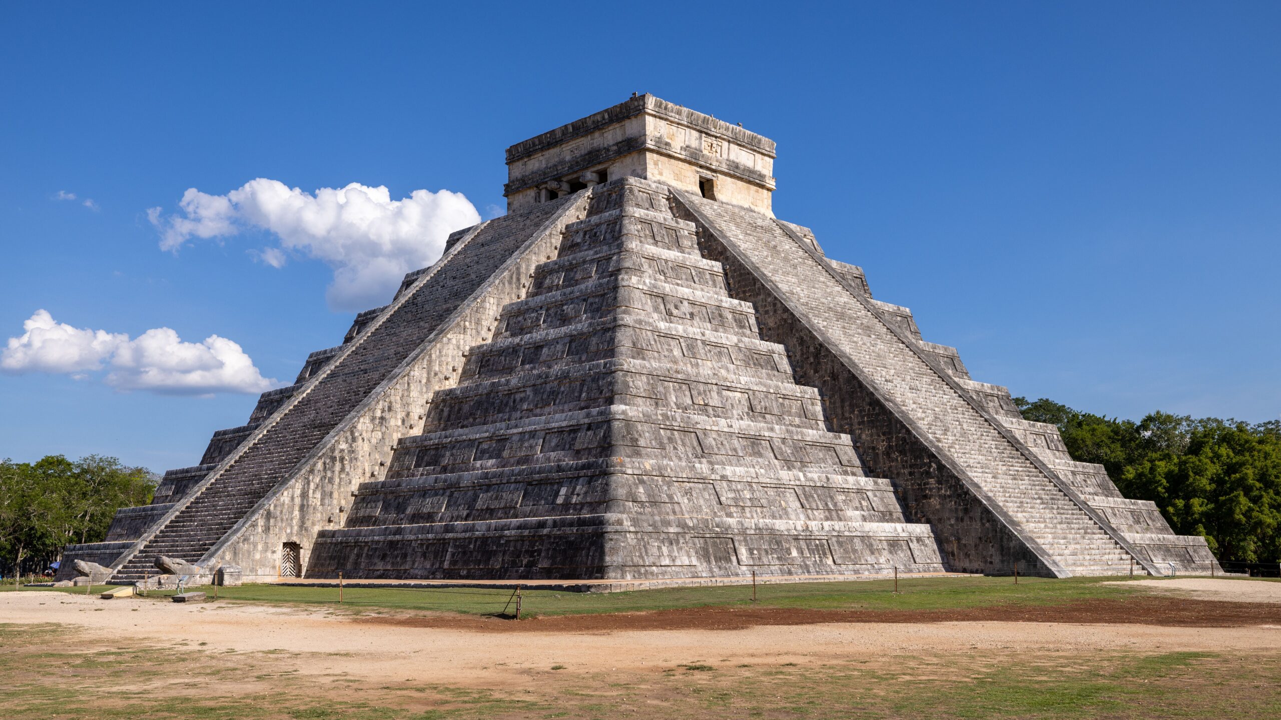 Vista en ángulo de la pirámide escalonada de Kukulkán en Chichén Itzá con cielo azul despejado y pocas nubes.