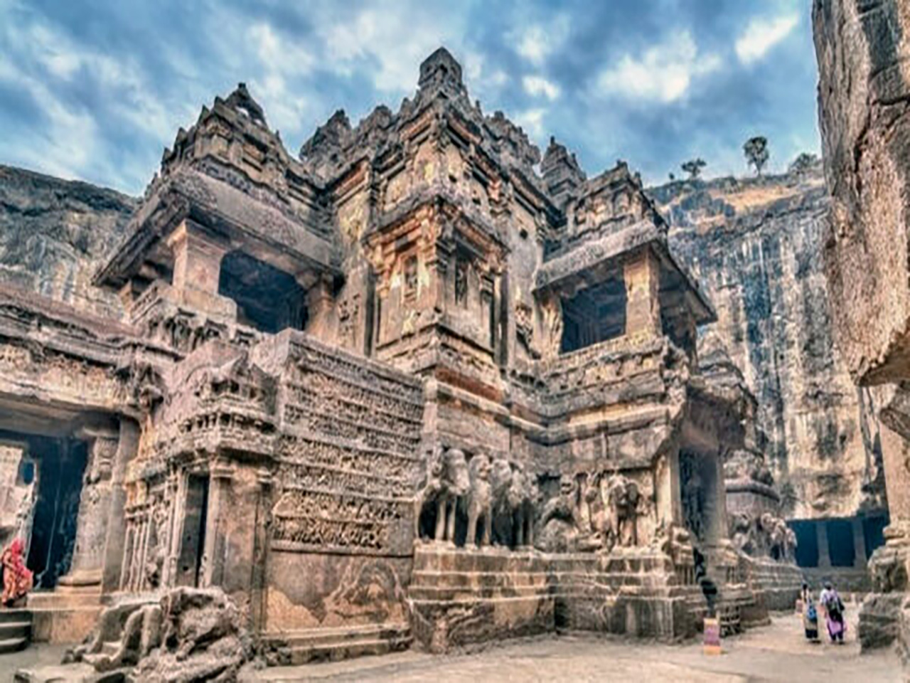 Vista en contrapicado de la intrincada fachada de piedra del Templo de Kailasa en Ellora, excavado directamente en el acantilado rocoso bajo un cielo dramático.